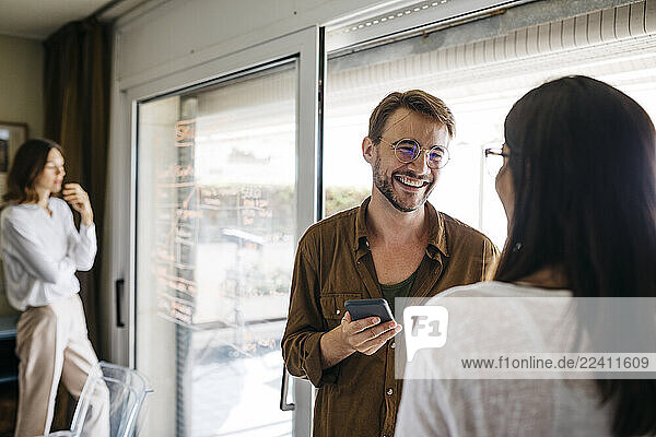 Happy coworkers with woman writing on glass pane in background