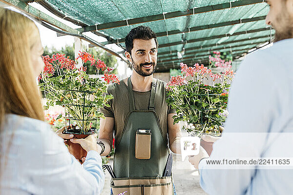 Smiling worker in a garden center showing plants to customers