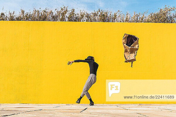 Young man dancing in front of yellow wall