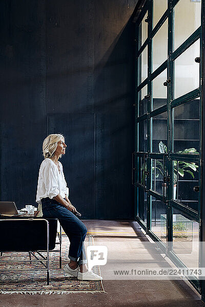 Casual mature businesswoman looking out of window in loft office