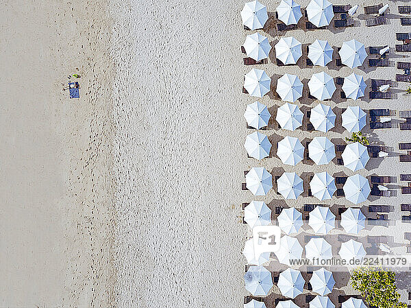 Indonesia  Bali  Aerial view of man sunbathing in front of rows of beach umbrellas on sandy coastal beach of Nusa Dua