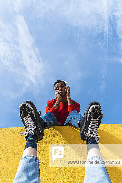 Young man with headphones  dancing for person  leaning on yellow wall