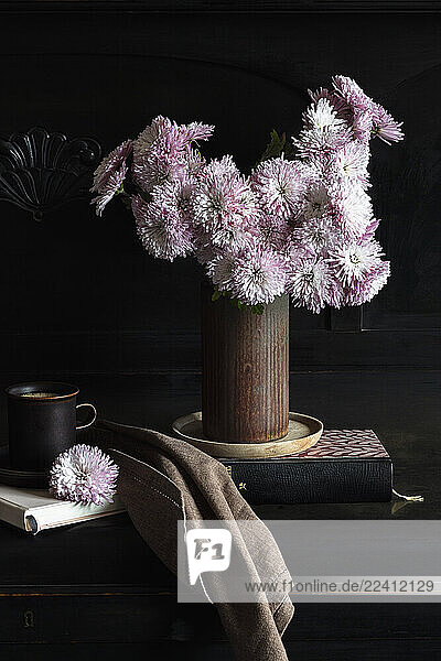 Bouquet of chrysanthemum in a rustic vase with a coffee cup and books in a studio setting