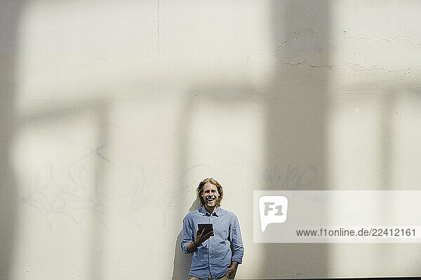 Laughing young man with tablet at a wall