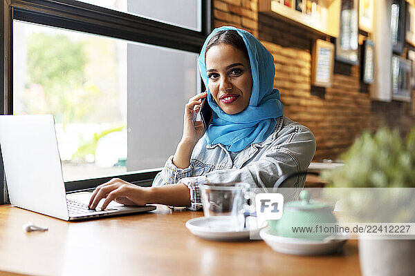 Businesswoman wearing turquoise hijab in a cafe and working with her laptop  on the phone