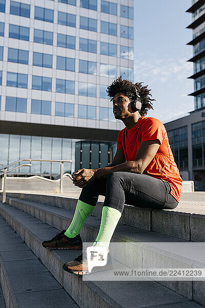 Young sportsman sitting on steps  using smartphone and listening to music