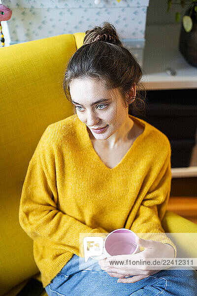 Young woman in a yellow armchair at home  enjoying tea and thinking