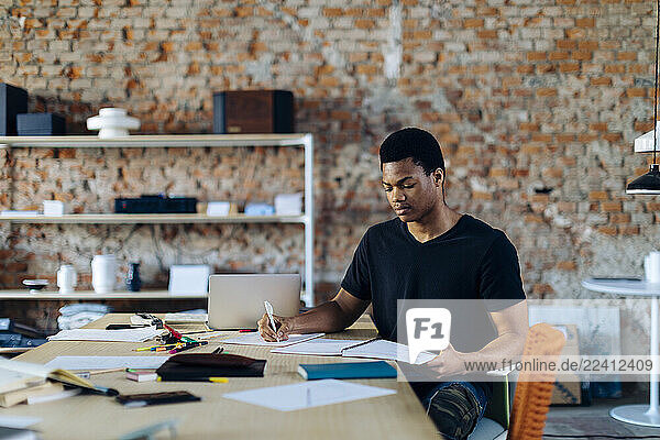 Young man sitting at table taking notes