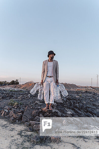 Young man holding empty plastic bottles in barren land