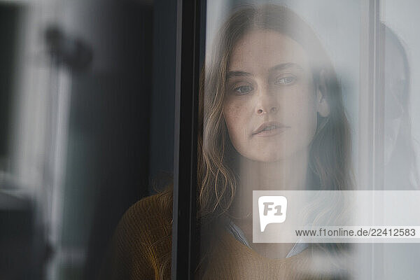 Pensive woman looking through a window with a thoughtful expression