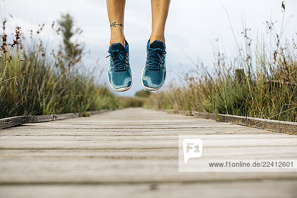Feet of female jogger  jumping on a wooden walkway