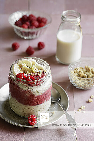 Raspberry-banana overnight oats in a glass jar with oat milk and granola in a studio setting