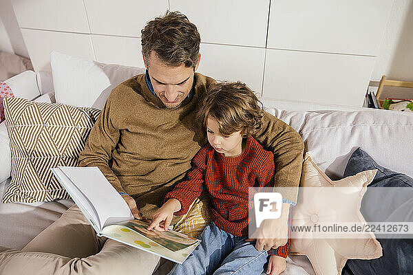 Father reading book with daughter on couch