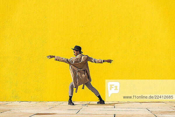 Young man dancing in front of yellow wall