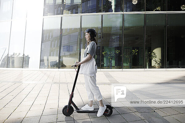 Woman with e-scooter and helmet  modern office buildings in the background