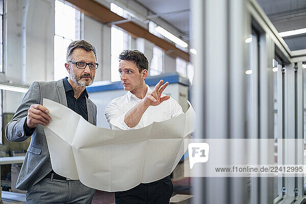 Two men discussing a blueprint in a production hall