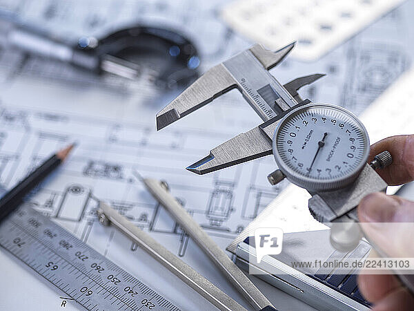 Close-up of a hand using calipers on a technical drawing for engineering measurement and quality control