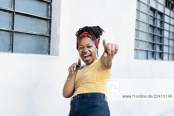 Portrait of excited young woman listening music with headphones and earphones in front of white wall