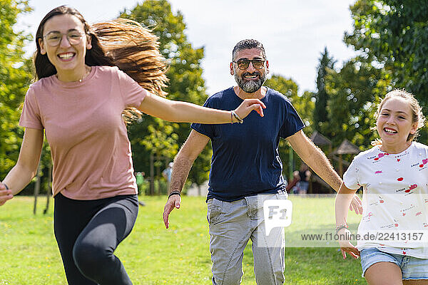 Carefree father with two daughters running on a meadow