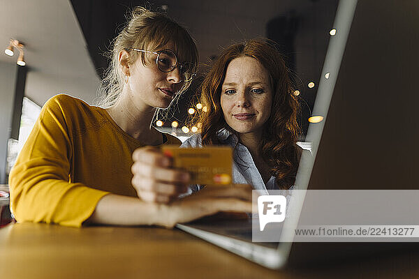 Two female friends with laptop and credit card in a cafe