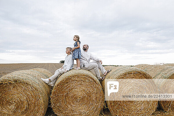 Father and his children sitting on hay bales  watching sky