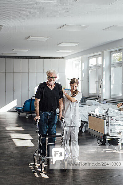 Nurse assisting patient with walker in clinic for rehabilitation