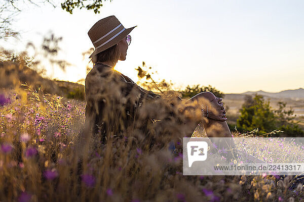 Young woman sitting on meadow at sunset
