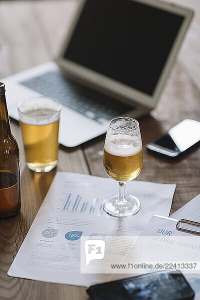 Beer bottle  glasses  documents and laptop on table