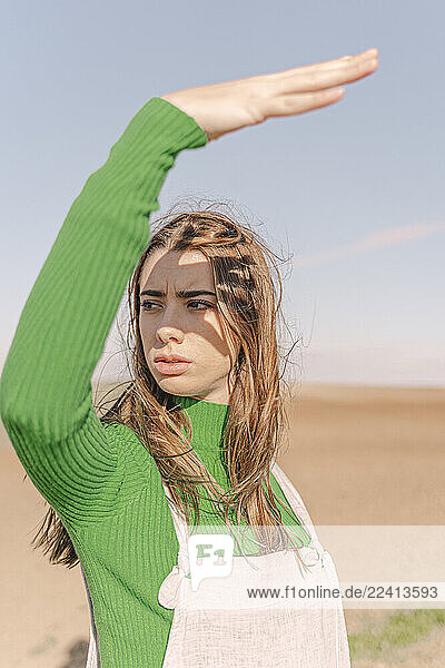 Young woman standing on dry field  shielding eyes