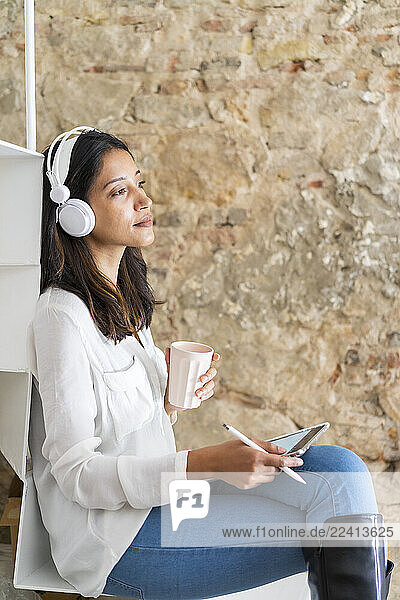 Portrait of young architect with headphones  digital tablet and coffee mug sitting on steps in a studio
