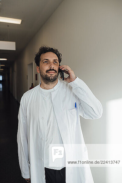 Doctor in a white coat having a phone call in a clinic hallway