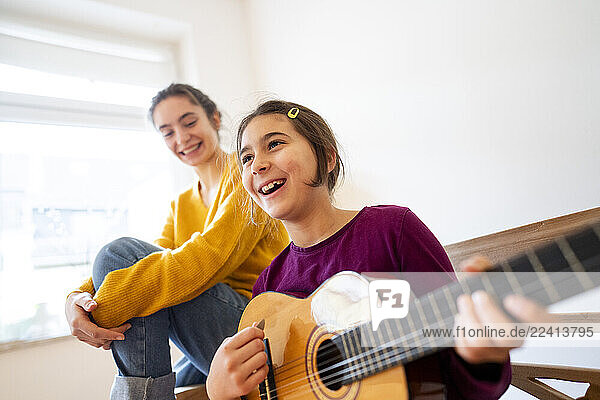 Big sister and little sister playing guitar and singing at home