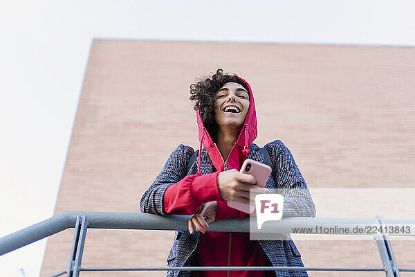 Portrait of laughing young woman mobile phone leaning on railing