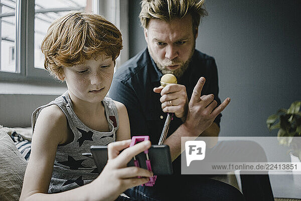 Father and son with smartphone and microphone at home