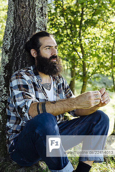 Man with beard sitting at tree trunk in the forest