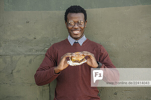 Young man eating cheeseburger  smiling