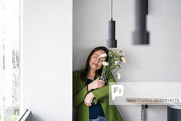 Woman in a café hugging a vase of flowers with a peaceful expression