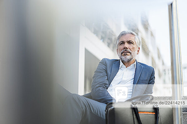Mature businessman sitting on stairs in the city looking around