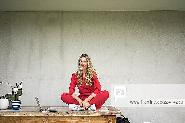 Smiling woman with laptop sitting on wooden table at home