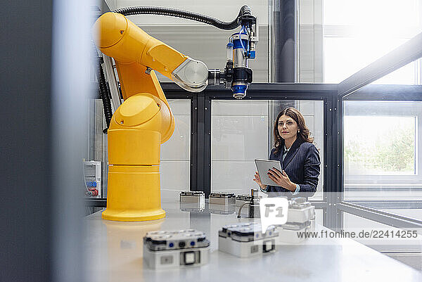Woman in a production hall with an industrial robot holding a tablet