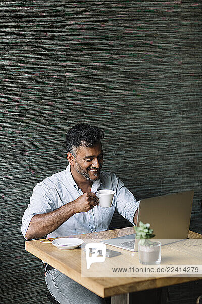 Smiling casual businessman using laptop in a cafe