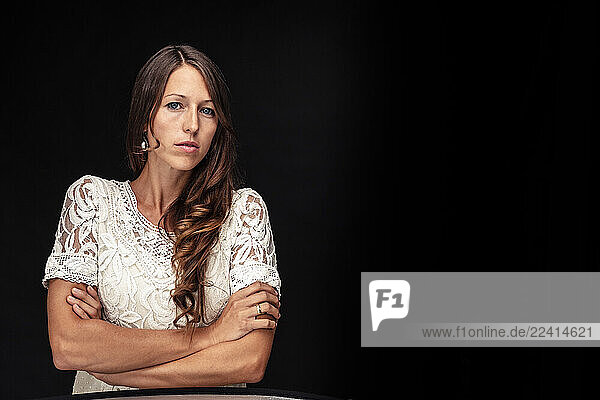 Portrait of young woman with arms crossed against black background