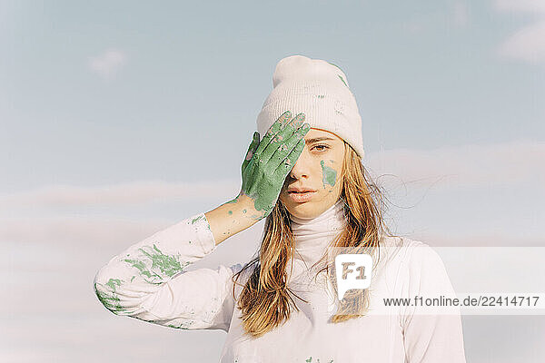 Young woman covering eye with green hand
