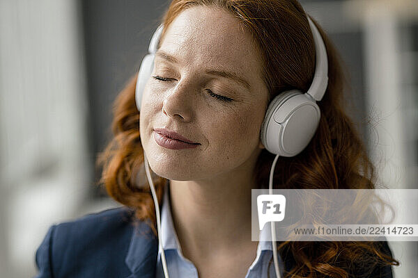 Portrait of redheaded businesswoman listening music with white headphones