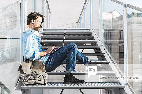 Casual businessman sitting on stairs using laptop