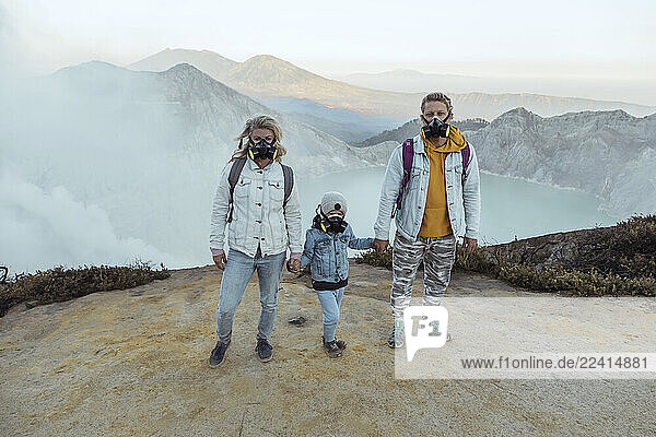 Family with respirator masks standing hand in hand at the edge of volcano Ijen  Java  Indonesia