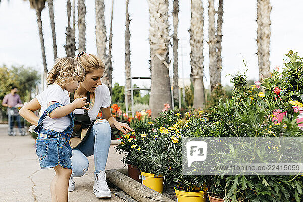 Female worker of a garden center showing flowers to a little girl