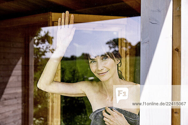 Portrait of smiling woman behind windowpane in a sauna