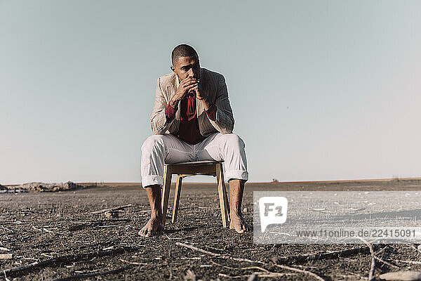 Young man sitting on chair in barren land