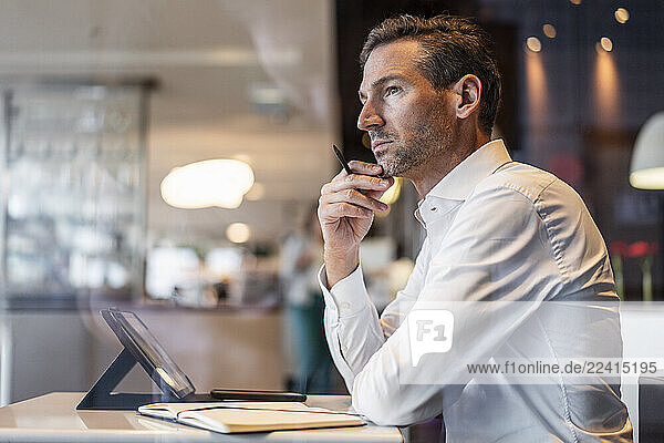 Thoughtful businessman in white shirt at office with tablet and notebook
